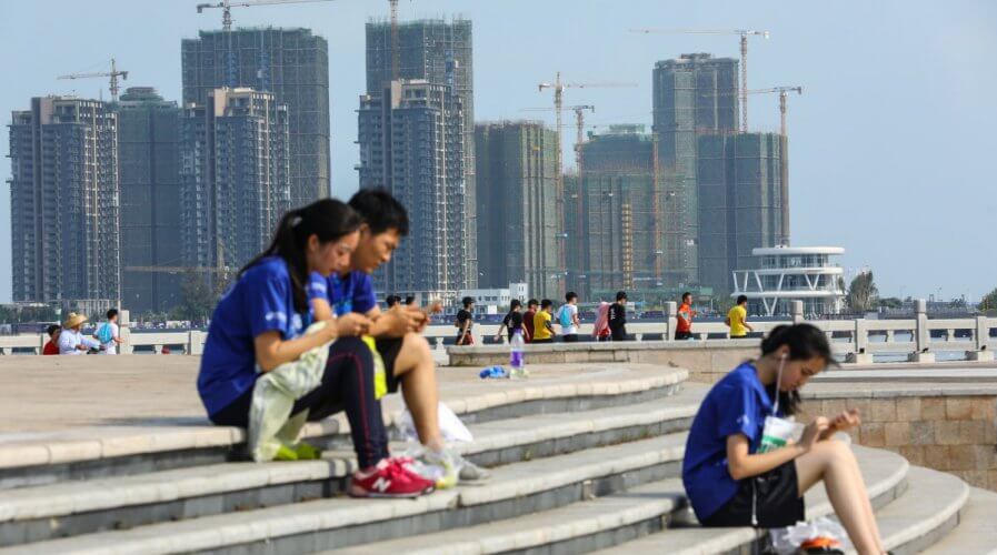 People sit on steps against a backdrop of residential buildings under construction, in Haikou, Hainan province, China