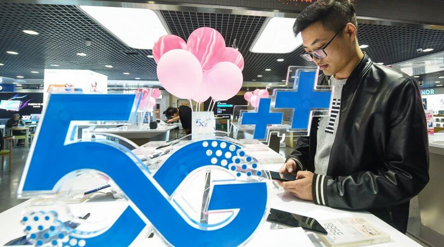 A customer looks at a mobile phone next to a 5G logo at a store in Hangzhou in China