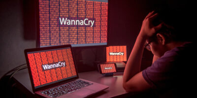 Young male frustrated, confused and headache by WannaCry ransomware attack on desktop screen, notebook and smartphone, cyber attack internet security concept