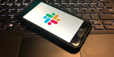 Slack App is open on a smart phone on top of a computer keyboard. Slack is a cloud based set of team collaboration software tools and online services.
