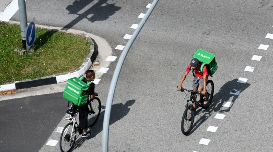 Grab delivery cyclists ride past each other in Singapore on April 20, 2020. (Photo by ROSLAN RAHMAN / AFP)