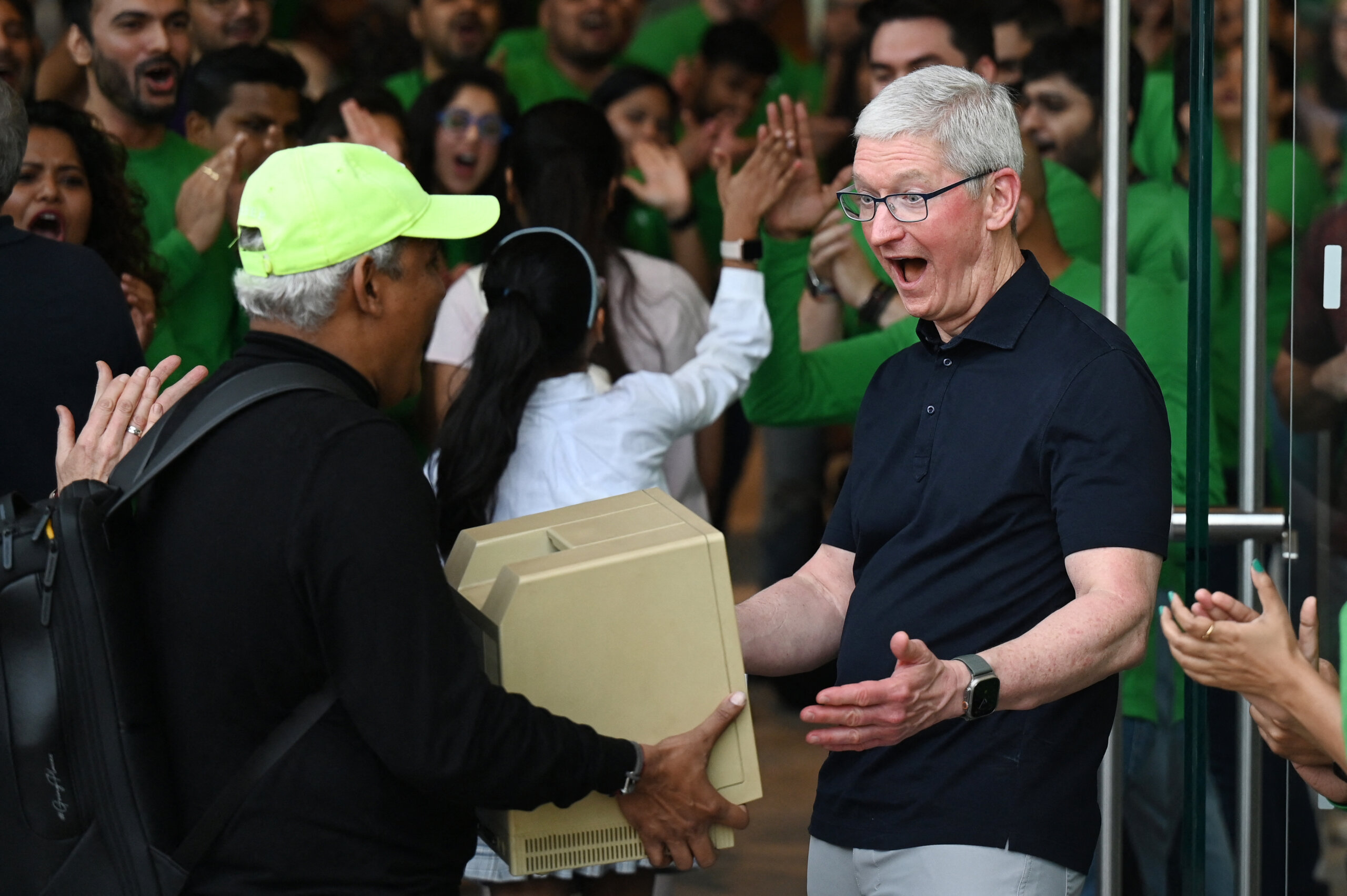 Chief Executive Officer of Apple Tim Cook (R) reacts as a man shows him a Macintosh SE computer during the opening of Apple's first retail store in India, in Mumbai on April 18, 2023. - Apple opened its first retail store in India on April 18, underscoring the US tech titan's increasing focus on the South Asian nation as a key sales market and alternative manufacturing hub to China. (Photo by Punit PARANJPE / AFP)