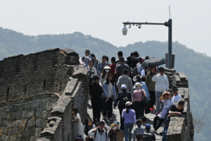 People walk below a surveillance camera on the Great Wall of China at Mutianyu, north of Beijing, on the Labour Day holiday on May 1, 2023. (Photo by GREG BAKER / AFP)